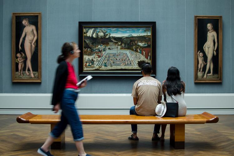 Un couple assis sur un banc dans un musée et une personne avec un audioguide.