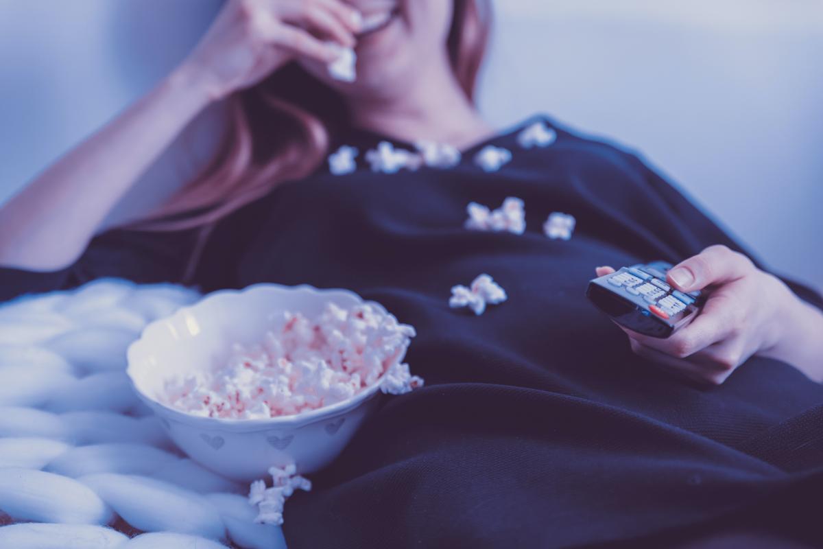 personne assise mangeant du popcorn, télécommande à la main