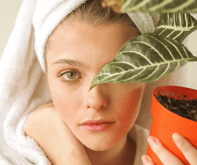 Une femme en peignoir de bain qui prend soin de sa peau et qui tient une plante dans la main