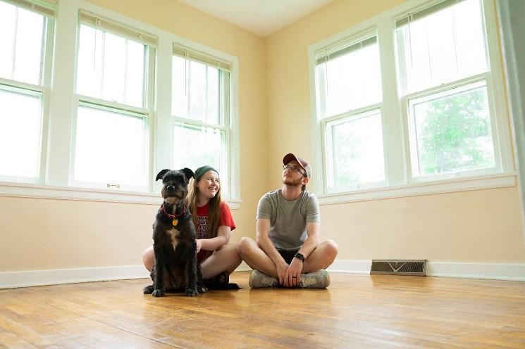 un homme, une femme et un chien assis à même le sol dans une pièce vide