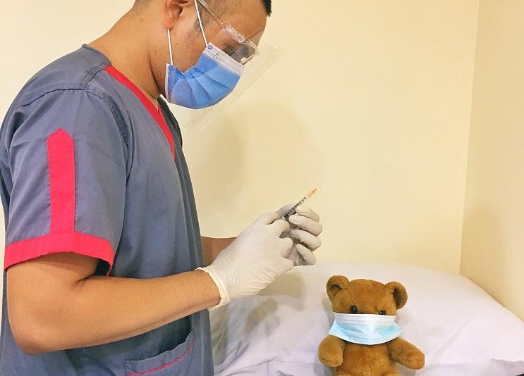 Un docteur avec un masque hygiènique, tenant une seringue, avec une peluche