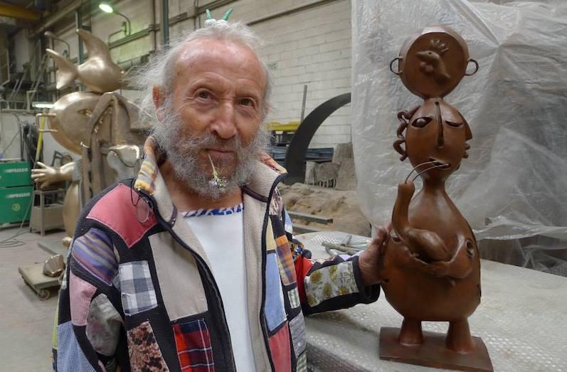 Un homme avec une barbe et des cheveux blancs devant une statuette en bronze