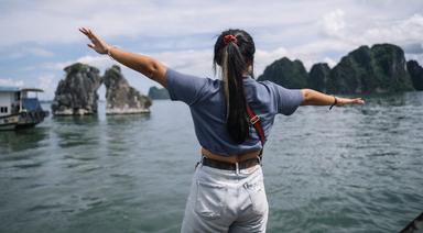 Une femme de dos écartant les bras face à la Baie d'Ha Long