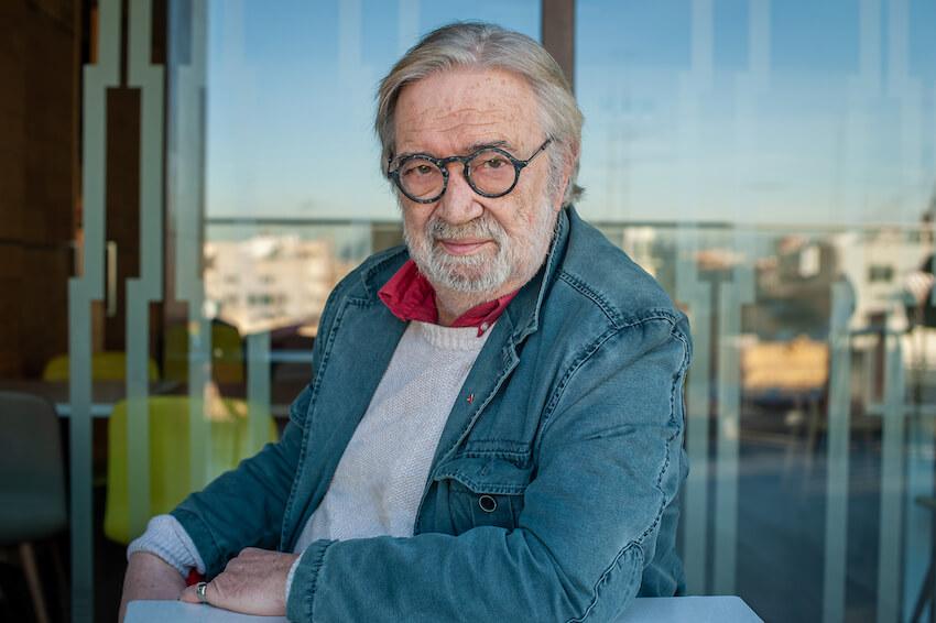 un homme assis avec des cheveux blancs et avec des lunettes rondes 