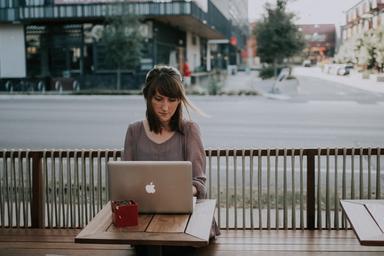 Une jeune femme teletravaille à une terrasse de café au soleil