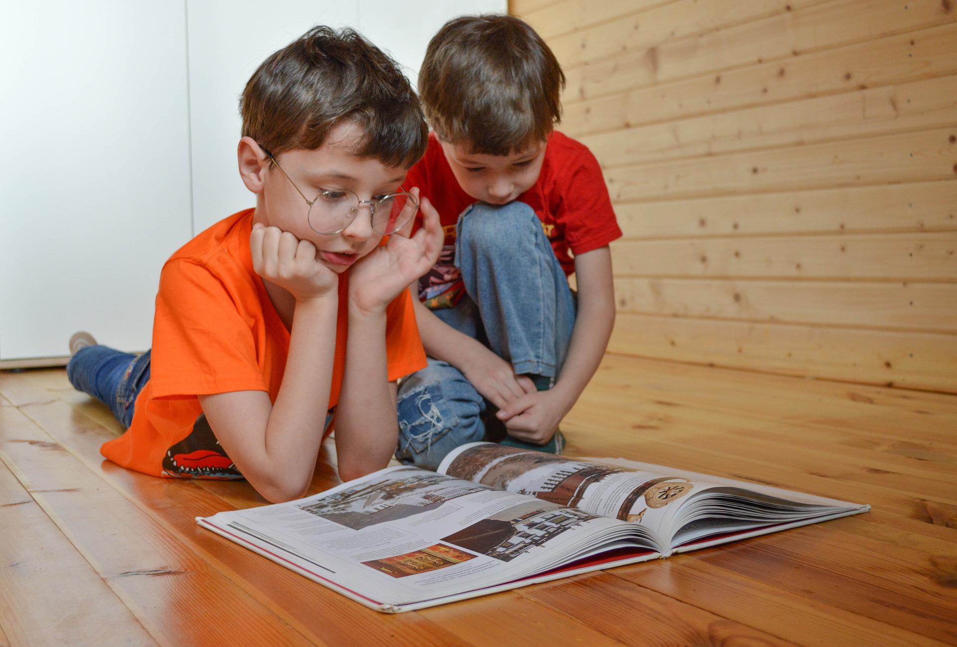 deux enfants sont assis par terre et lisent un livre ensemble 