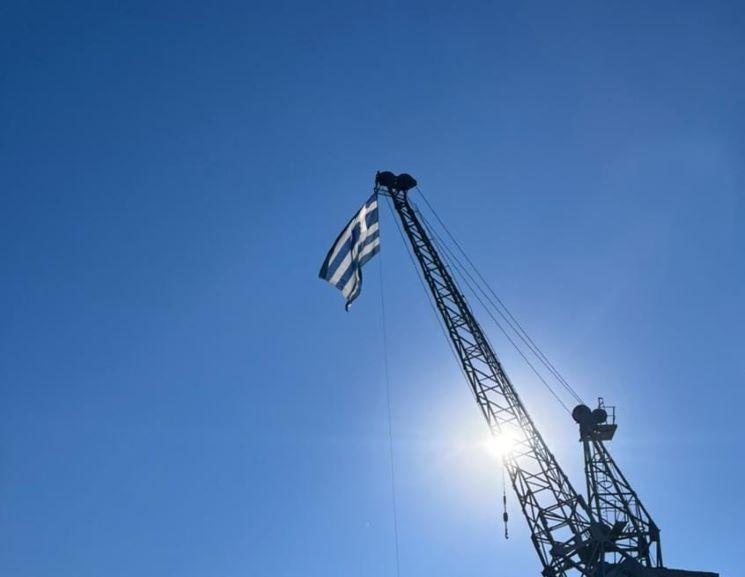 un drapeau grec qui flotte attaché à une grue