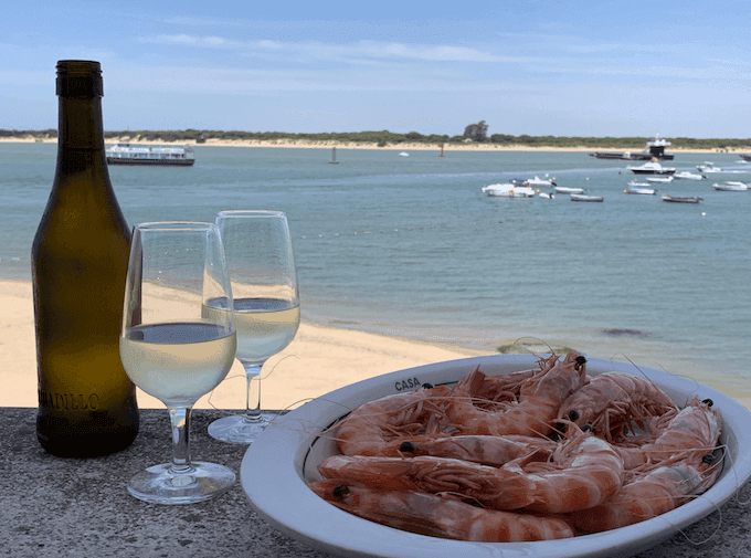 une bouteille de vin et des crevettes devant la mer