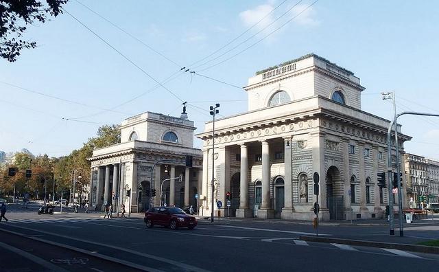 une voiture rouge circule devant les portes de Milan