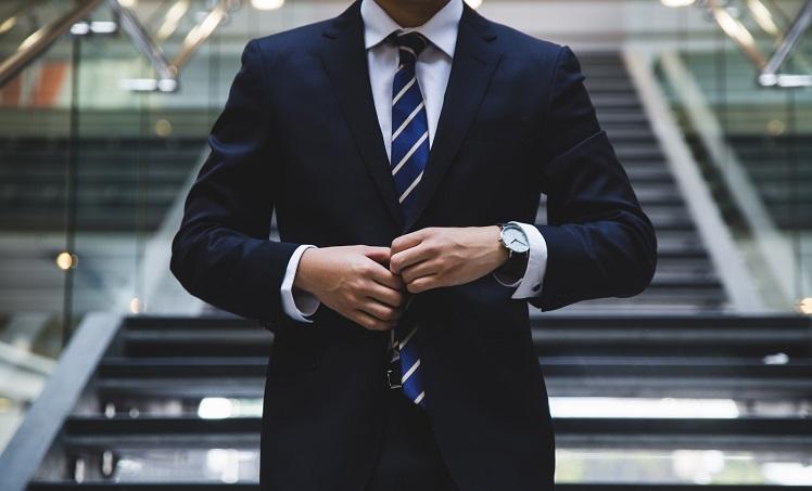 homme en costule cravate debout devant escaliers - hunters-race-unsplash