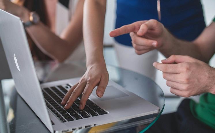 trois personnes travaillent sur un clavier et montrent du doigt écran d'ordinateur