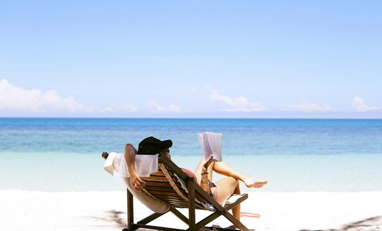 une femme lit un livre sur une chaise longue face à la mer bleu