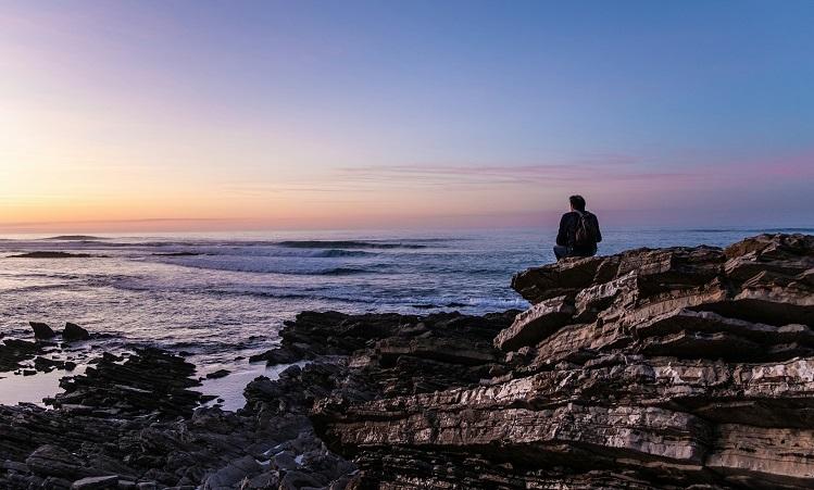 un homme refléchit assis sur un rocher face à la mer