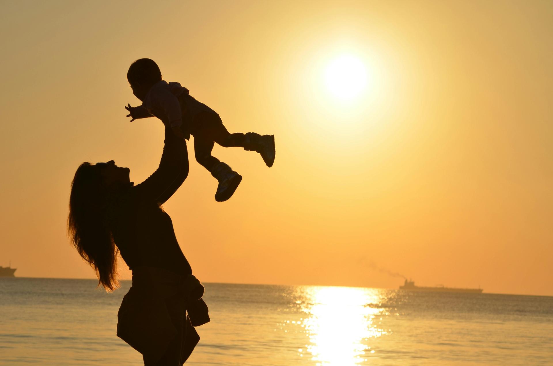 Parent porte un enfant sur une plage au couché de soleil