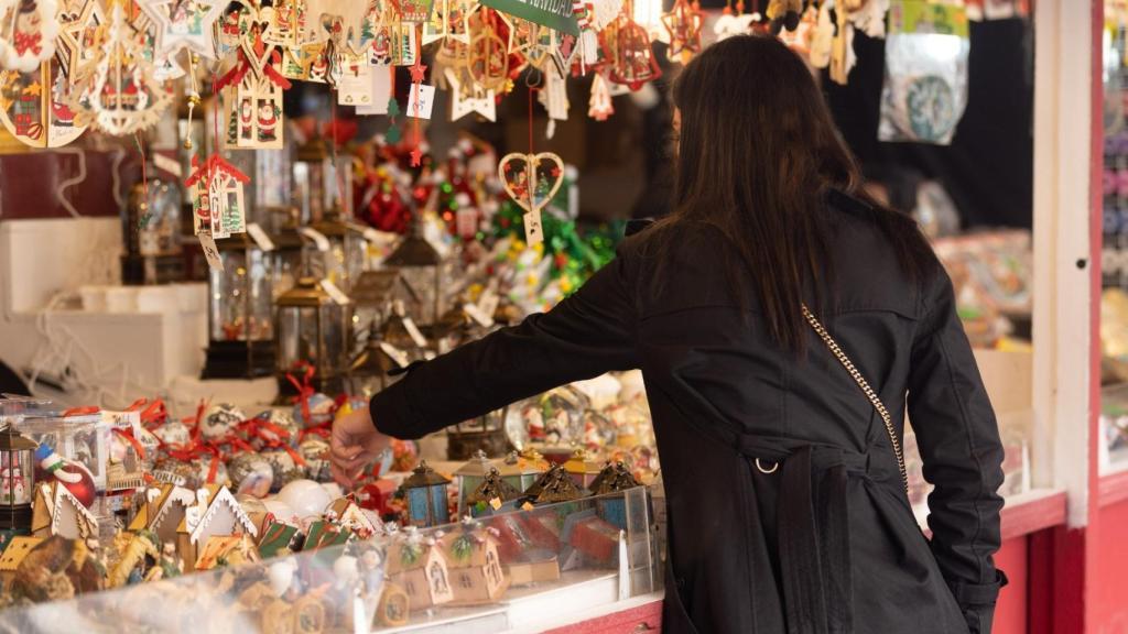 Une visiteuse explore les stands d’artisanat au marché de Noël, parmi une multitude de décorations et de cadeaux faits main, créant une ambiance festive et chaleureuse