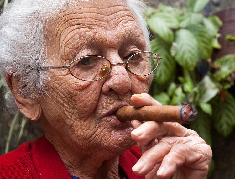 Une femme âgée aux cheveux blancs et aux lunettes fumant un cigare