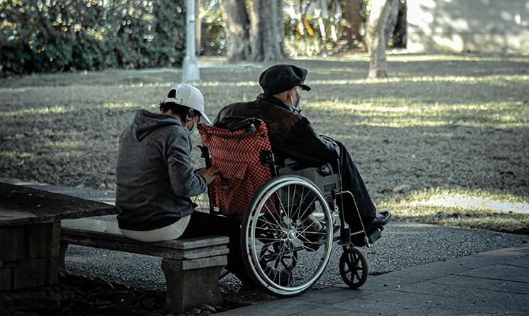 Un homme âgé dans un fauteuil roulant, accompagné d'une personne sur un banc