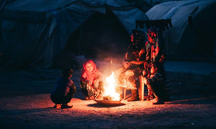 Deux femmes et deux filles assises autour d'un feu à côté de tentes