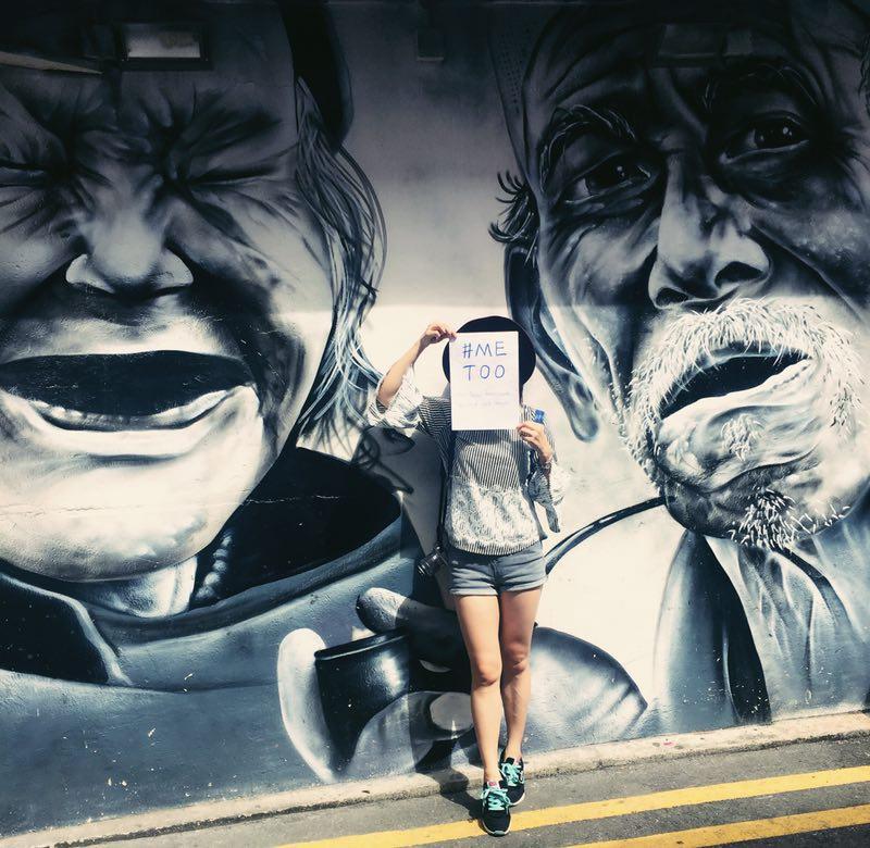 Une femme avec une feuille #metoo devant une fresque murale 