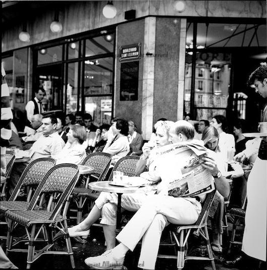 des personnes sur une terrasse d'un café avec un homme en train de lire