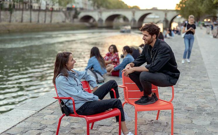 Des jeunes qui parlent sur les quais de Paris assis sur des chaises Fermob 