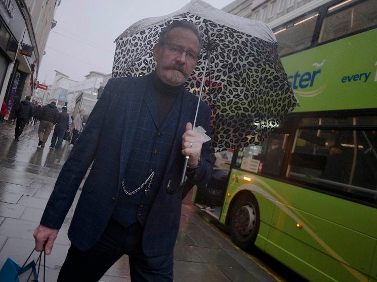 Un homme en costume à carreaux sous la pluie, face à l'objectif