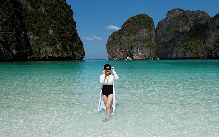 Une touriste patauge dans l'eau cristalline sur la plage de Maya Bay en Thailande