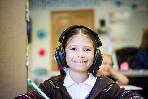 une petite fille sourit en écoutant de la musique en classe 