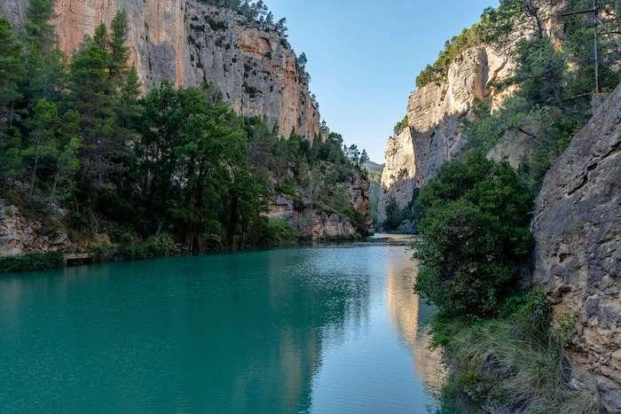 lac entouré d'arbres verts et de montagnes rocheuses brunes à Montanejos