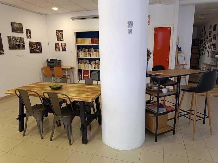 la salle principale de la base culture à valencia avec une table des chaises un pilier et la bibliothèque au fond