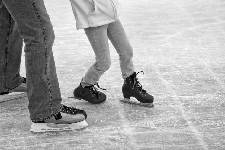 Un adulte et un enfant patinant main dans la main sur une patinoire, en noir et blanc