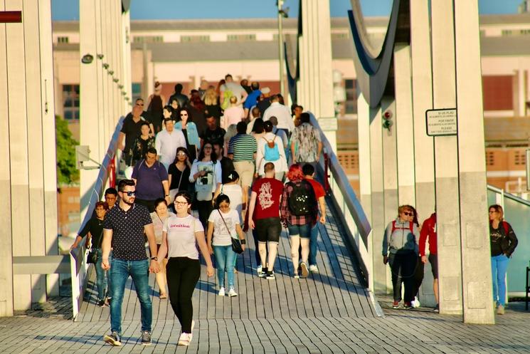 Un grand groupe de personnes traversant un pont animé sous le soleil