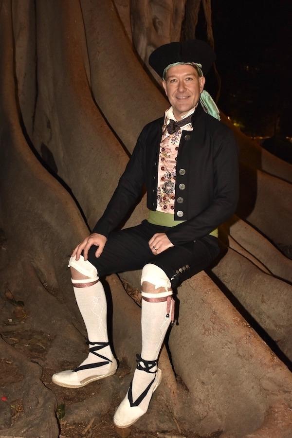 un homme assis sur un arbre avec un costume noir